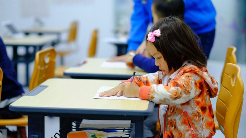 A young student sits at a desk with a pencil in her hand.