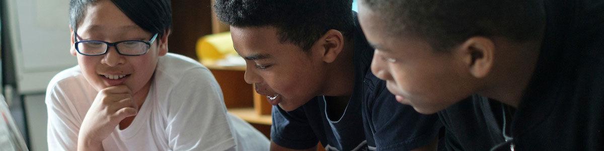 Three middle school age students talk together in a classroom.